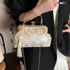 A beige embroidered silk evening clutch with gold chain straps held against a black blazer.