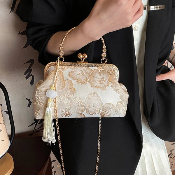 A beige embroidered silk evening clutch with gold chain straps held against a black blazer.
