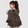 A woman is shown wearing a brown leopard print backpack while standing against a light gray background.