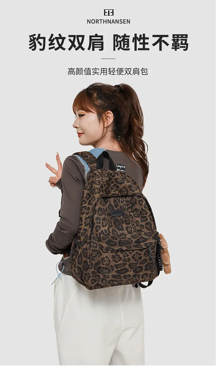 A woman is shown wearing a brown leopard print backpack while standing against a light gray background.