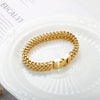 A close-up of a chunky gold link chain bracelet worn on a white plate.