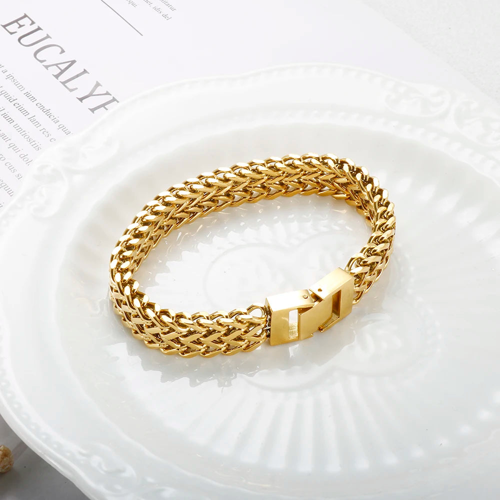 A close-up of a chunky gold link chain bracelet worn on a white plate.