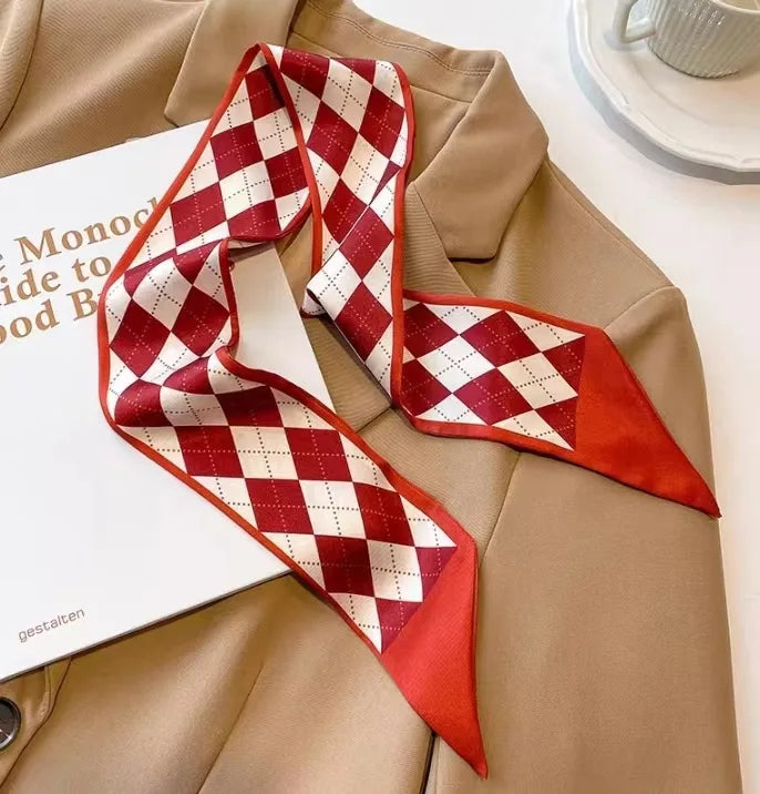 Écharpe de soie à carreaux rouges et blancs drapée sur un blazer beige à côté d'une boîte blanche.