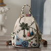A handcrafted linen backpack featuring floral embroidery and a woven handle, resting on a wooden surface.