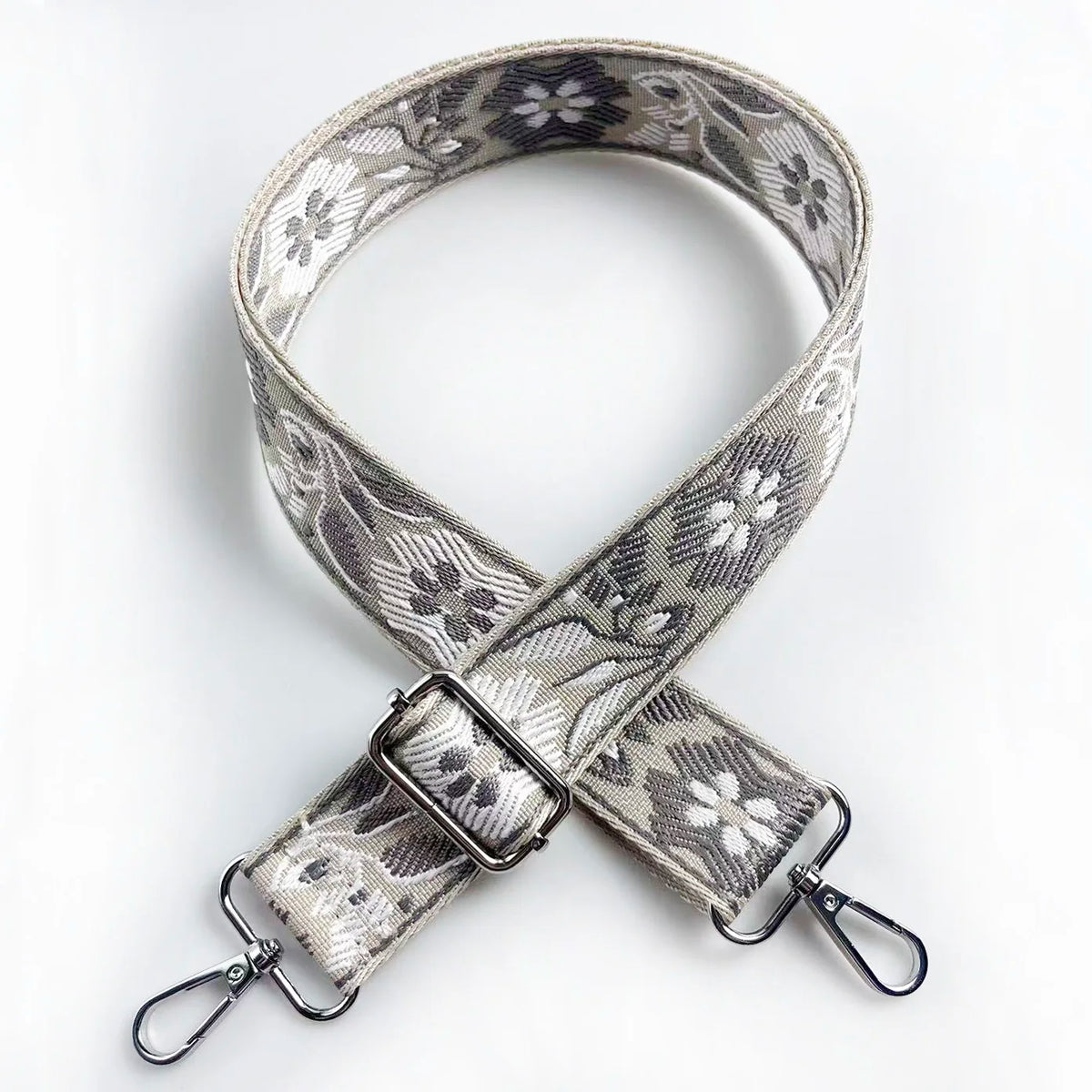 A beige and gray patterned jacquard strap for a crossbody bag, featuring a silver buckle.
