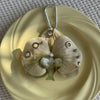 A realistic pale green orchid flower keychain with a silver loop, displayed on a light yellow plate.