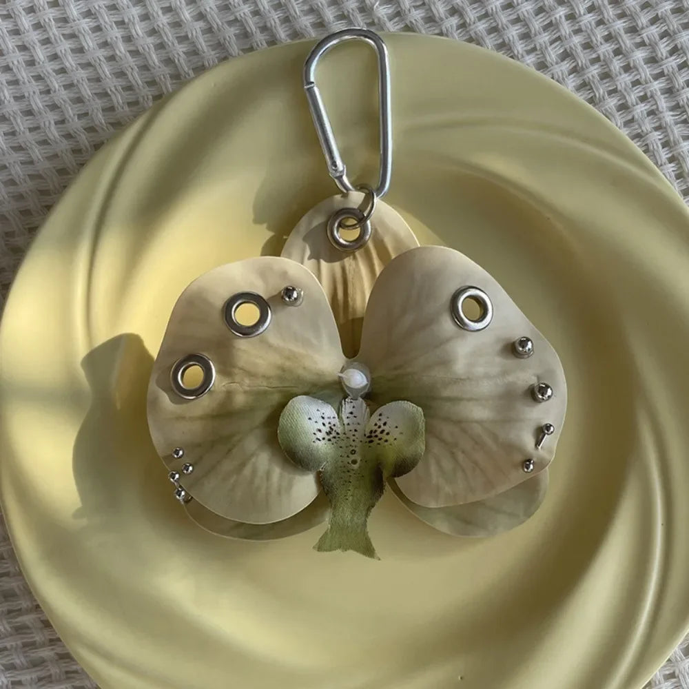 A realistic pale green orchid flower keychain with a silver loop, displayed on a light yellow plate.