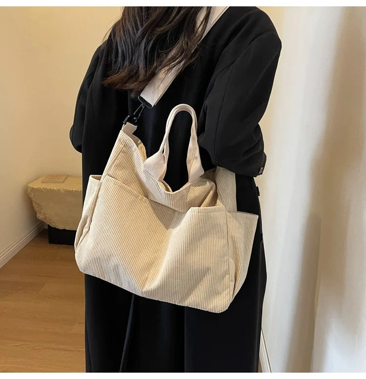 A woman holds a beige corduroy multi-pocket tote bag against a black outfit.