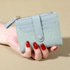 A hand holds a light mint green PU leather card wallet with a double zip closure.