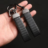 A close-up of a black carbon fiber leather keychain with silver metal hardware being held in a hand.