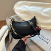 A black shoulder bag with gold chain detailing and a cherry pendant resting on a light gray fabric.