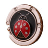 Ganchillo para mesa de mariposa de metal dorado rosa con diseño negro y rojo.
