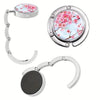 Silver bag hook with a circular floral design and a separate round silver component.