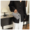 A person holds a striped crochet tote bag with a shell accent against a dark wooden table.