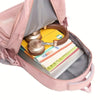 A pink travel backpack is open, showing a yellow notebook and a gold-colored pen inside.