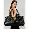 A woman holds a black vegan leather tote bag with gold hardware against a light gray background.