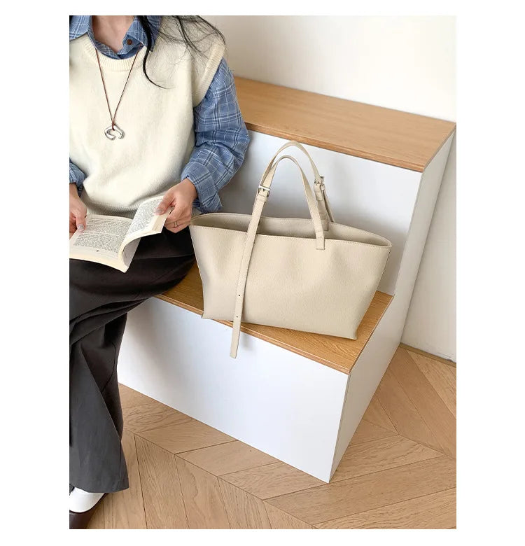 Un sac à main en cuir PU beige et décontracté est exposé sur une étagère en bois à côté d'une personne lisant un livre.