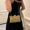 A woman holds a rectangular gold rhinestone evening clutch bag against a black dress.