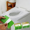 A hand holds a stack of green and white disposable toilet seat covers next to an open toilet seat cover dispenser.