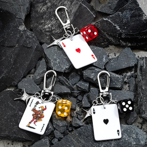 Un jeu de dés et de cartes de poker rétro sur colliers de clés argentés, posés sur des rochers sombres.