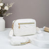 Weiße gesteppte Crossbody-Tasche mit goldfarzigem Reißverschluss und Trageriem auf weißem Untergrund.