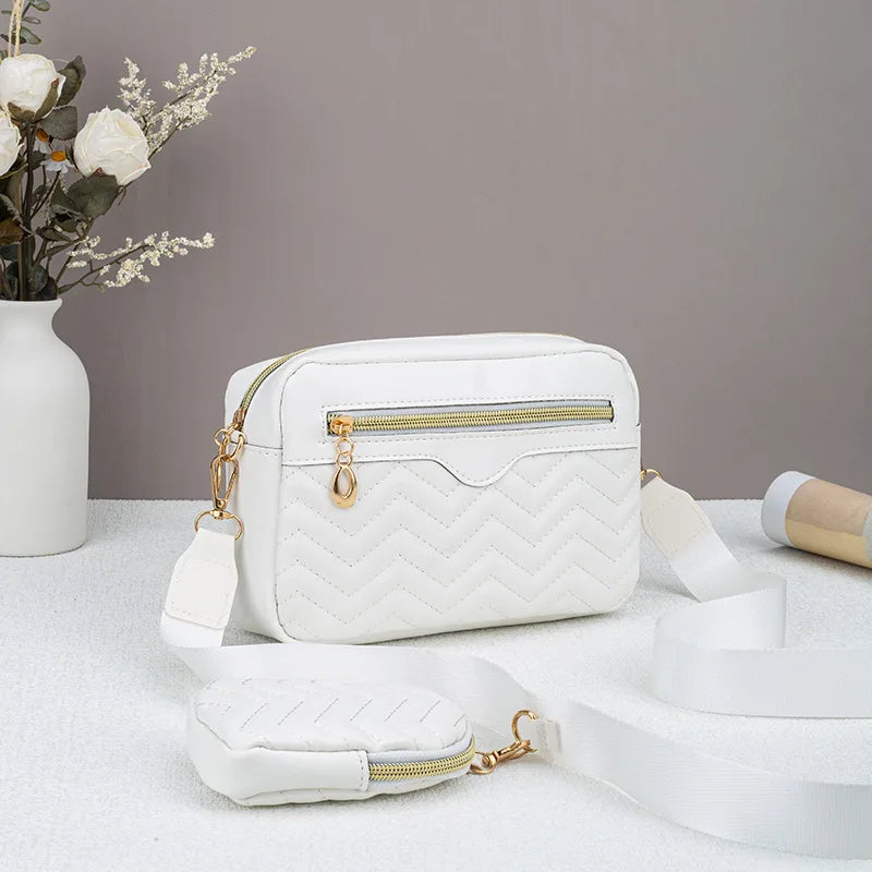 Weiße gesteppte Crossbody-Tasche mit goldfarzigem Reißverschluss und Trageriem auf weißem Untergrund.