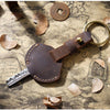 A brown leather key fob cover with a keychain ring rests on aged parchment paper.