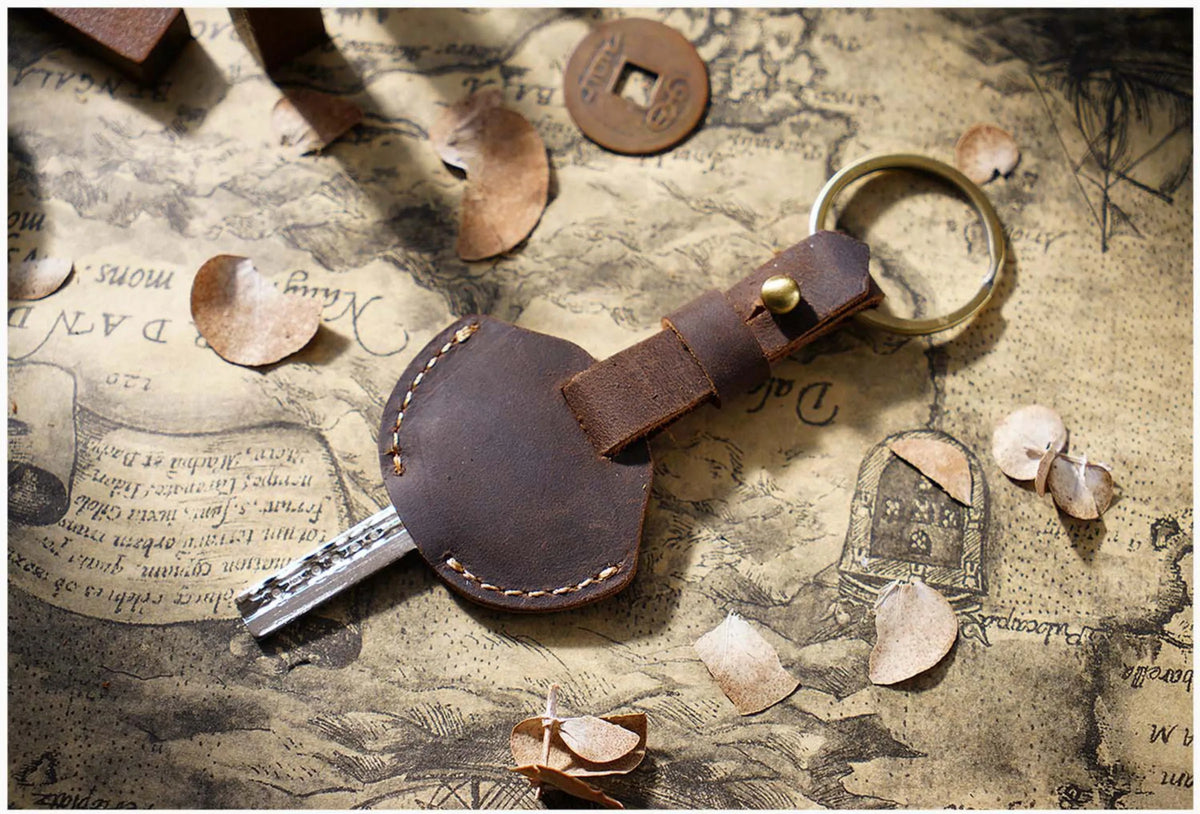 A brown leather key fob cover with a keychain ring rests on aged parchment paper.