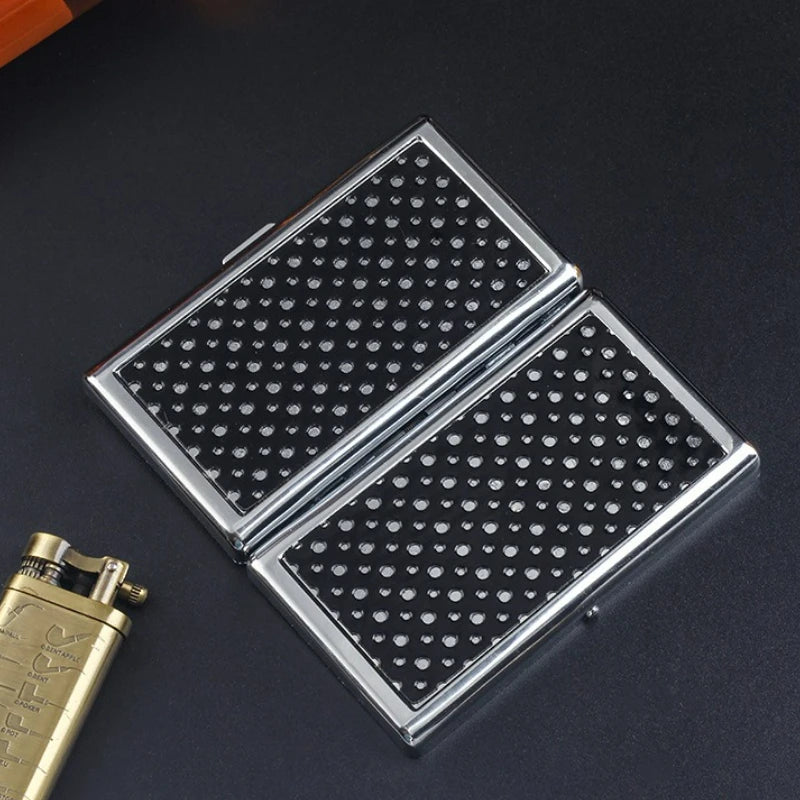 A silver metal cigarette case holder with a black patterned lid is shown on a dark surface.
