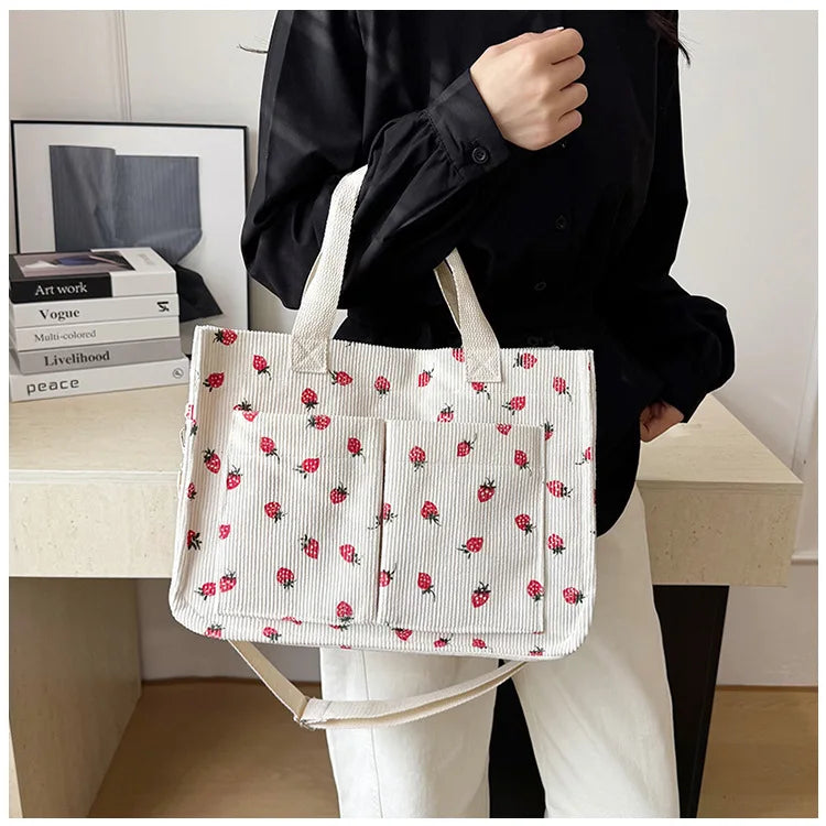 A woman holds a white canvas tote bag with a red strawberry pattern against a light background.