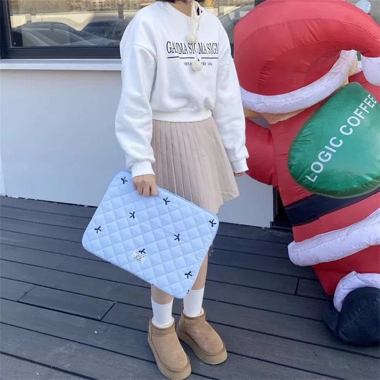 A person wearing a white sweatshirt and beige skirt holds a light blue quilted laptop sleeve.