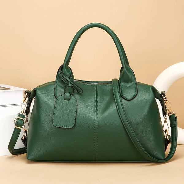 A dark green soft leather tote bag with a zipper closure and adjustable shoulder strap resting on a light surface.