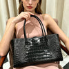 A woman holds a black crocodile embossed leather tote bag with a magnetic closure.