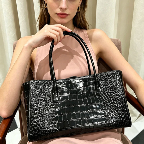 A woman holds a black crocodile embossed leather tote bag with a magnetic closure.