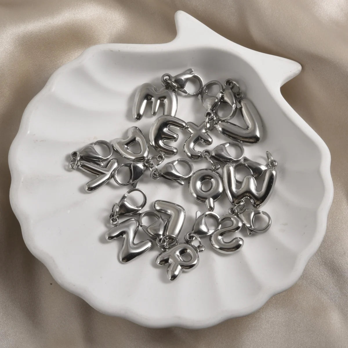 Silver stainless steel alphabet letter charms with lobster clasps arranged on a white dish