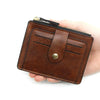 A brown leather card holder wallet with a zipper and coin pocket is held in a hand.