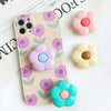 A light pink phone case featuring purple and green floral patterns, with several matching flower-shaped grips scattered nearb