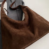 A brown suede slouchy shoulder bag with leather straps is shown against a gray background.