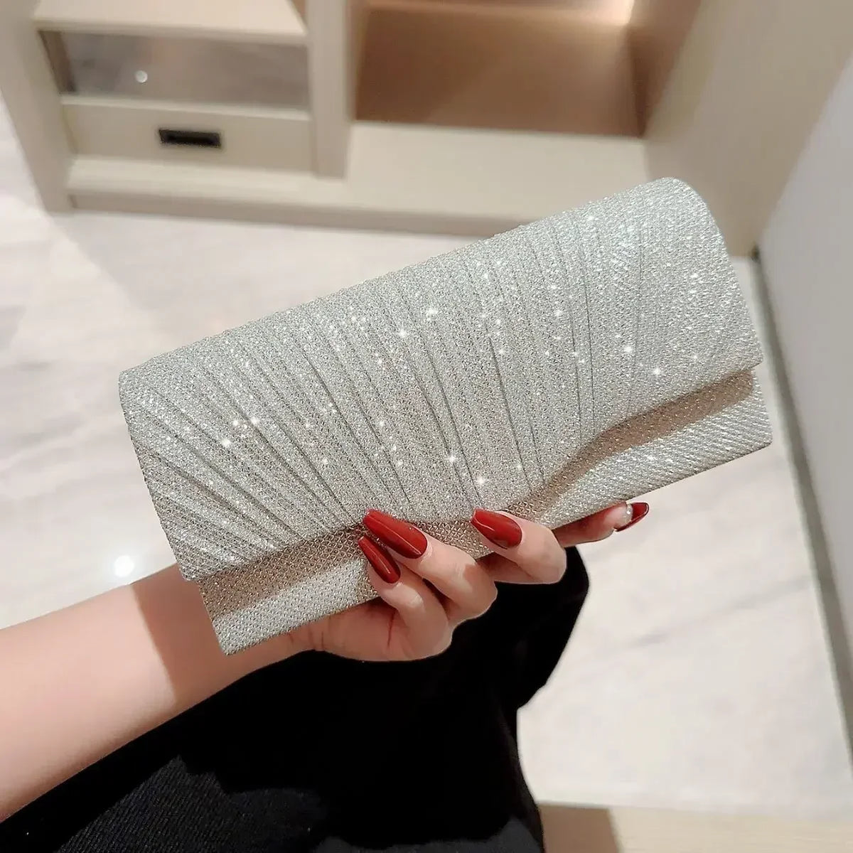 Eine Hand hält eine elegante silberne Ketten-Shoulder-Clutchtasche mit texturierter, schimmernder Oberfläche.