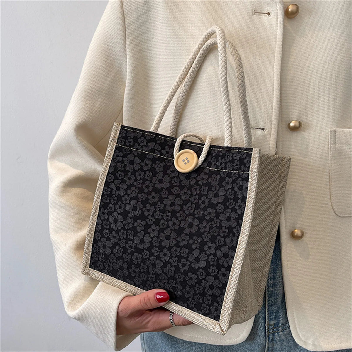 A beige blazer sleeve holds a black floral linen tote bag with natural twine closures.