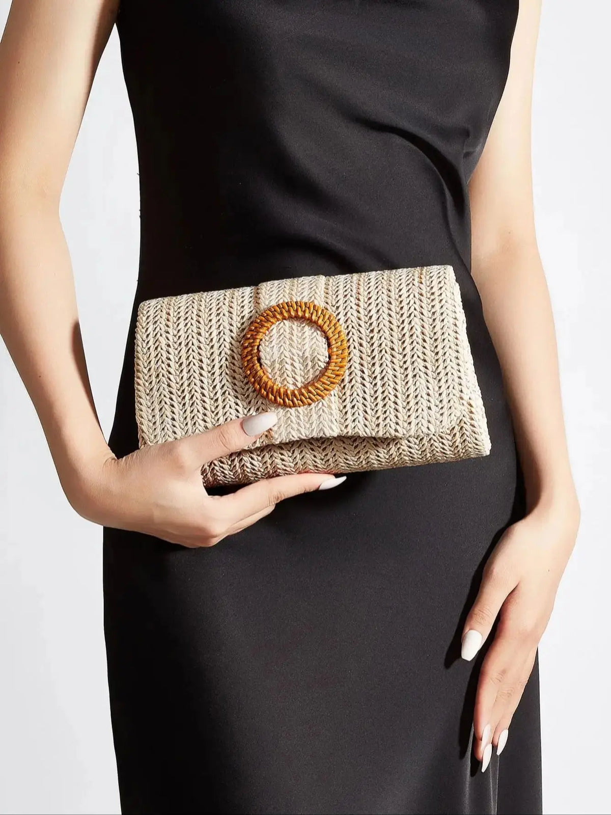 A woman holds a woven straw envelope clutch with an orange beaded strap against a black dress.