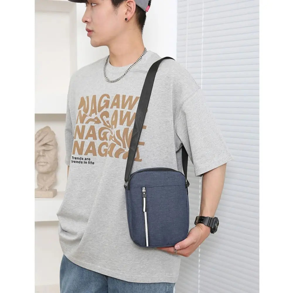 A man wearing a gray t-shirt holds a navy blue waterproof crossbody bag.