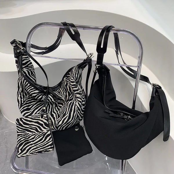 A black canvas zebra print shoulder crossbody bag displayed on a clear acrylic hanger.