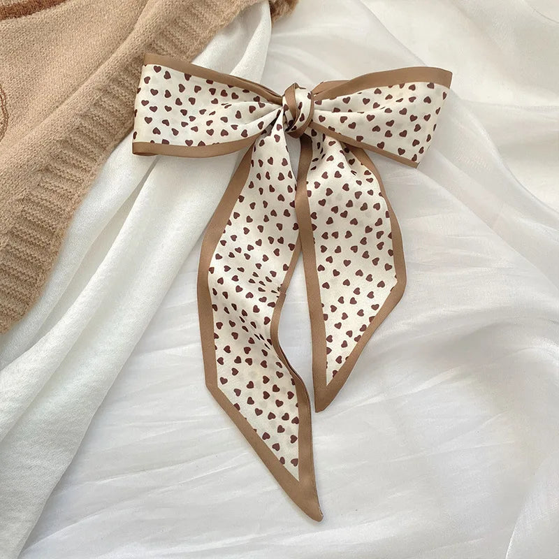 Foulard de cheveux en soie à motifs beige et marron, noué en nœud, sur tissu blanc.