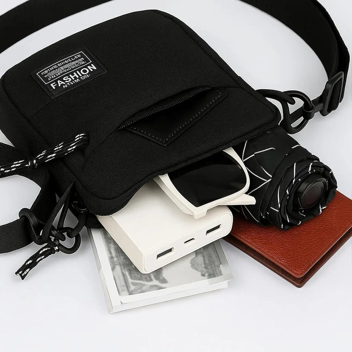 A black men's compact crossbody sling bag with a leather strap and accessories laid out on a white surface.