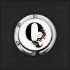 A silver, round letter Q with a floral design is shown against a dark background.