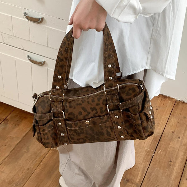 A brown leopard print shoulder bag with silver rivets being held by a person against a white background.