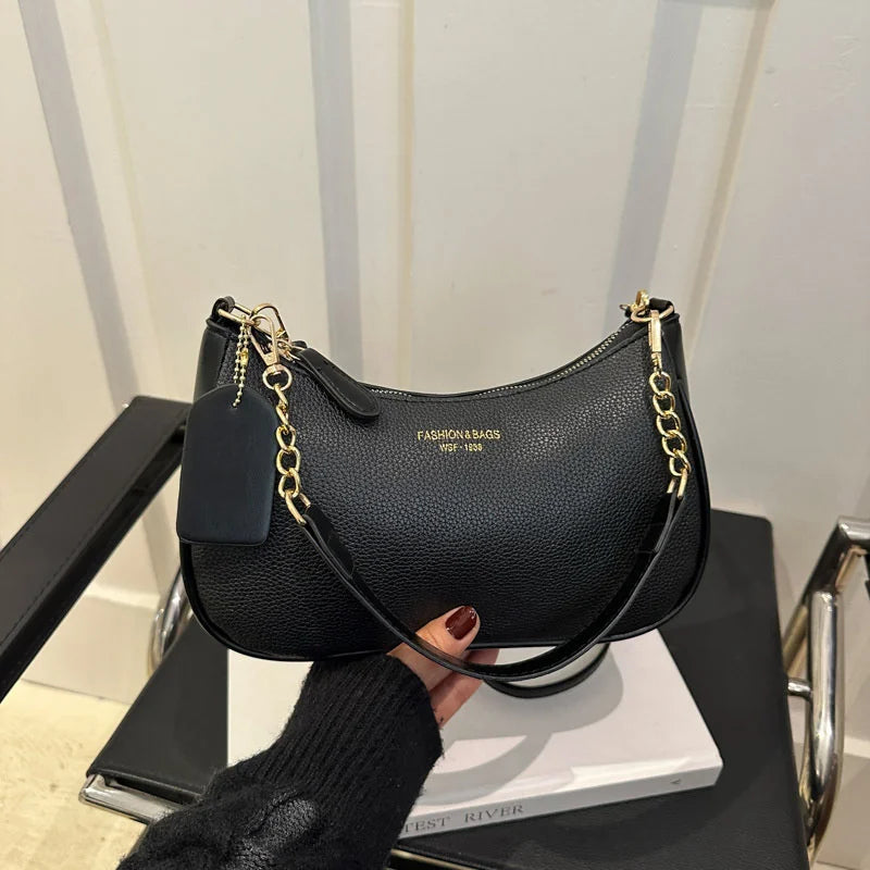 A black leather shoulder bag with gold chain detailing and a square flap is displayed on a dark surface.
