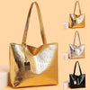 A gold metallic crocodile print zipper tote bag displayed against a beige background.