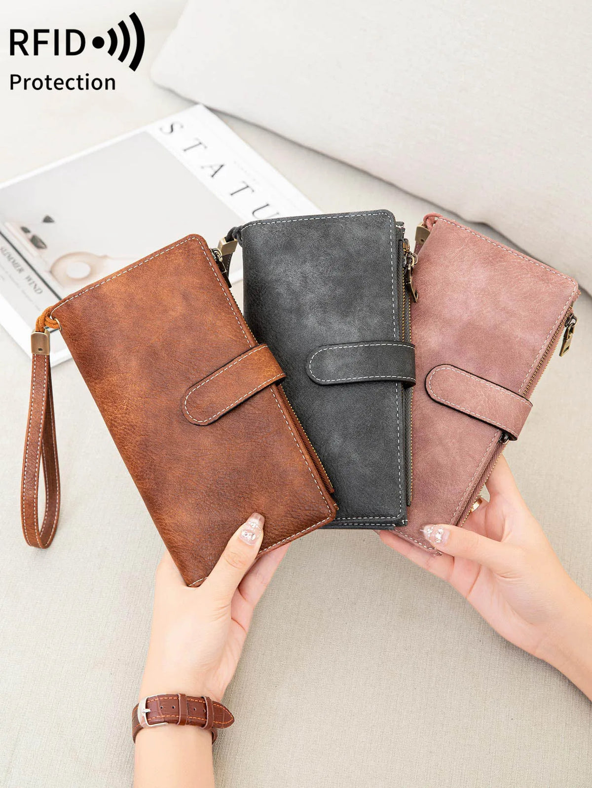 Three leather trifold clutch wallets in brown, gray, and pink colors being held by hands.